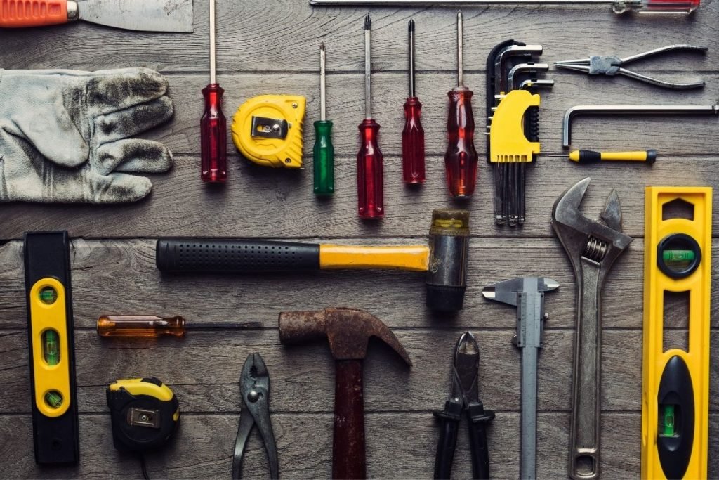 Tools scattered on a wooden table, featuring a mix of hand tools like drills, screwdrivers, and wrenches for various tasks.